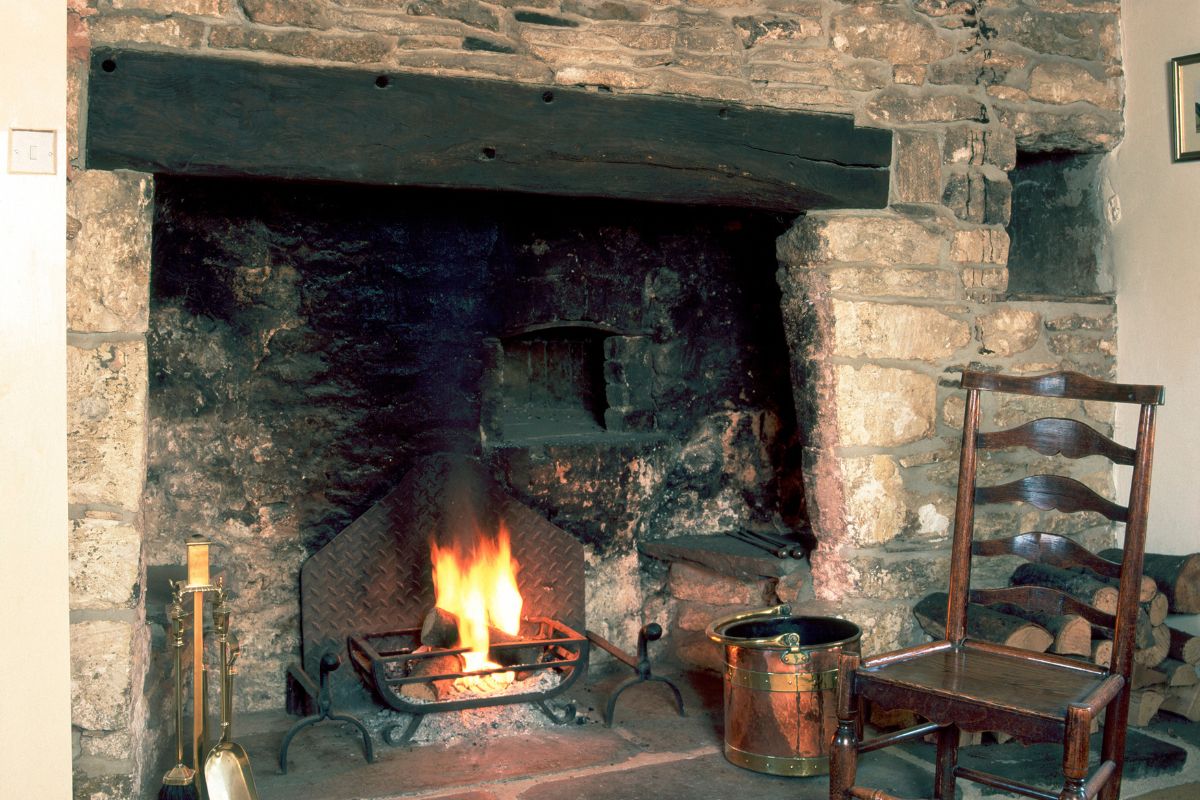 old looking fireplace with stone wall and wood burning fire