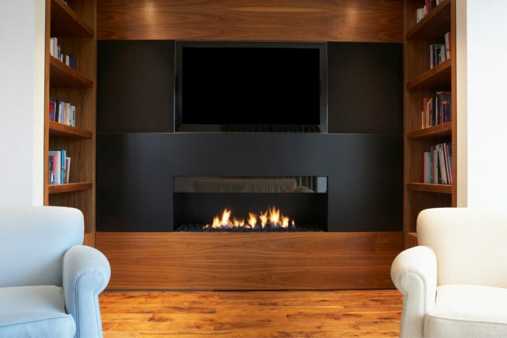 Fireplace below a tV with flames and book shelves o the sides