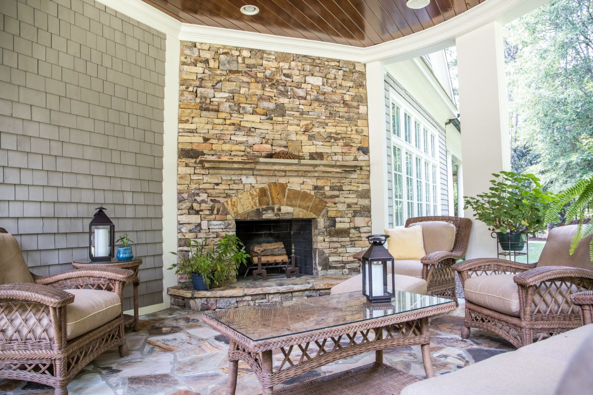 Modern Outdoor Fireplace with brick fireplace surround. Table and wicker chairs in front of the fireplace. Decorated with storm candles,