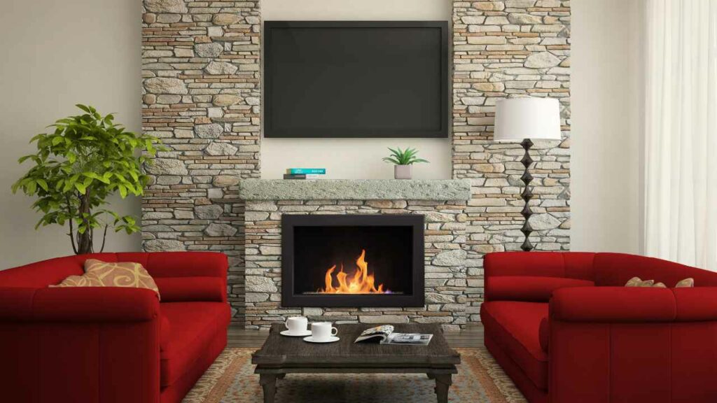 Gas burning fireplace, stone surround. TV above. Two red sofas either side and wood flooring.