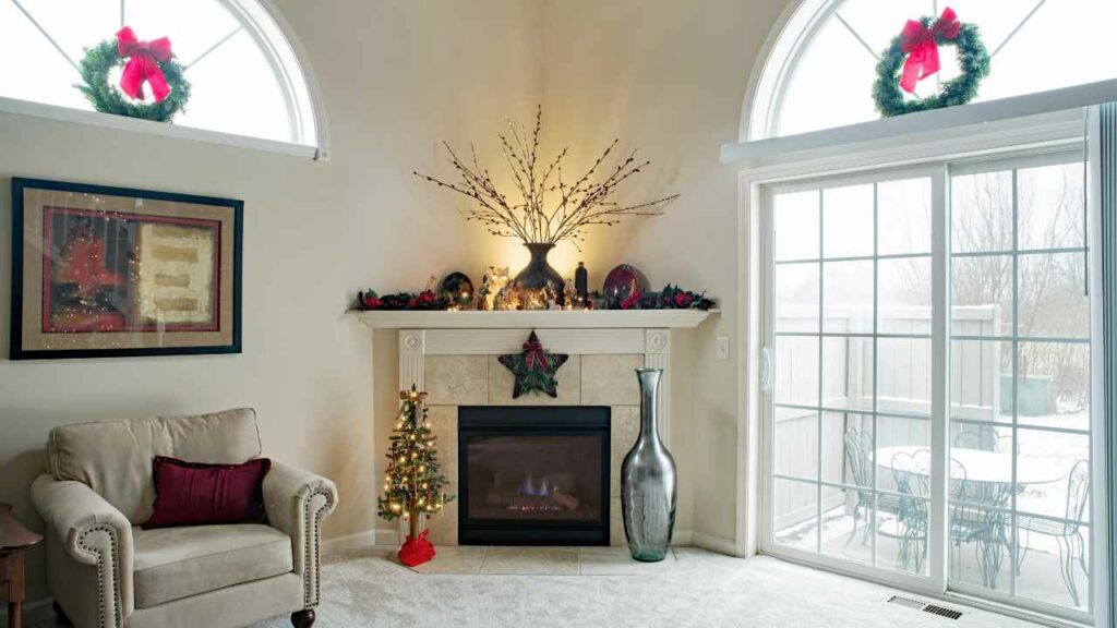 corner fireplace. cream gas fireplace. Christmas decorations on mantel. Large glass door to the backyard to the side.