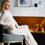 Electric Vapor fireplace. Young woman keeping warm in front sitting on chair.. Modern design. Photograph on mantel.