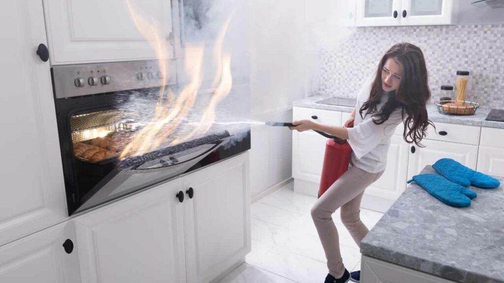 Woman using a fire extinguisher to put out an oven fire. large modern kitchen. food can be seen in the oven.
