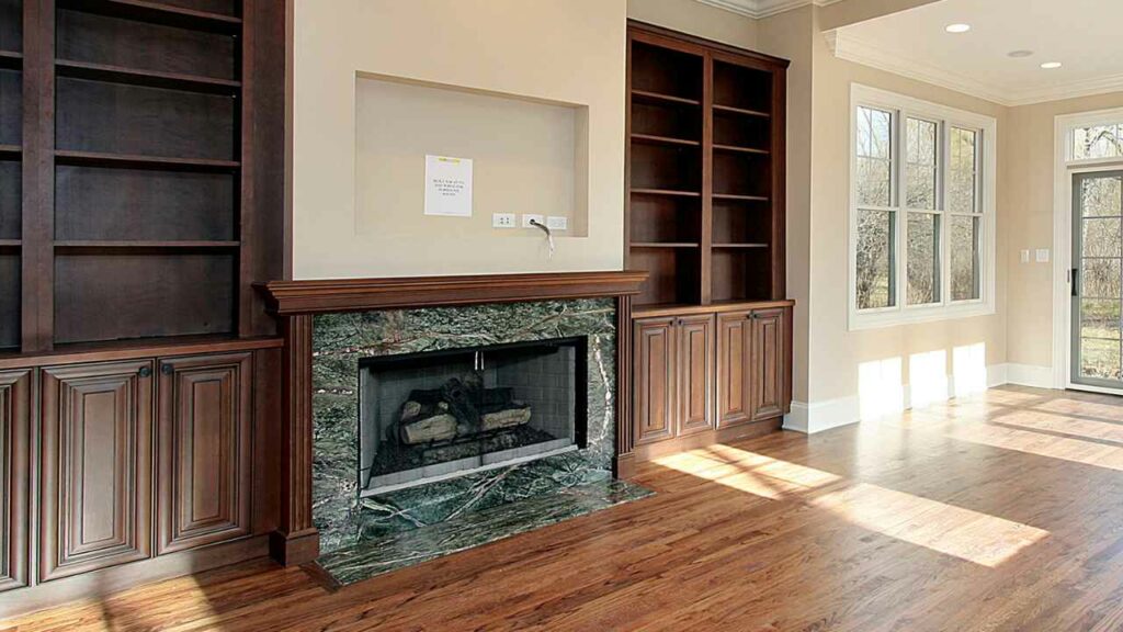 Dark green marble fireplace. Space for TV above. Wood book Shelves either side. Wood flooring.