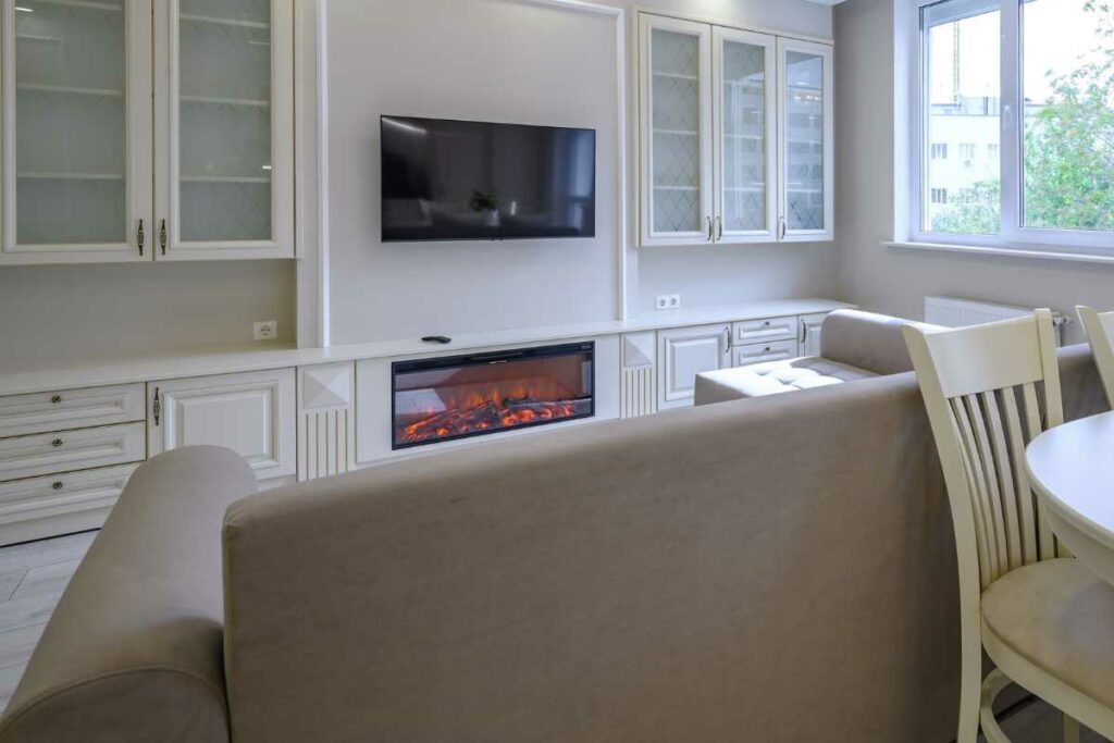 Electric fireplace insert below a tv. Sofa and glass shelving either side of the tv.