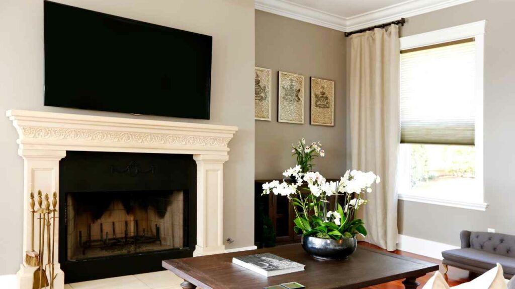 TV above fireplace. Flowers in front on small side table. pictures on the wall
