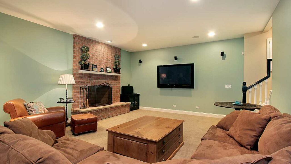 Basement fireplace with brick surround and mantel above the fireplace. two sofas surround fireplace.