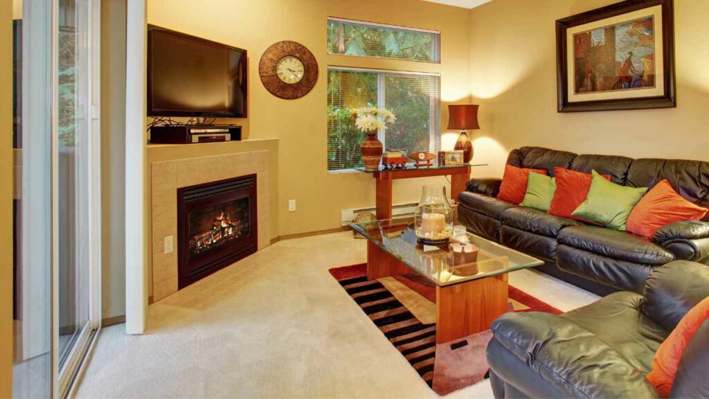 corner electric fireplace with cream til surround and matching hearth. Carpet. Leather sofa and side table.