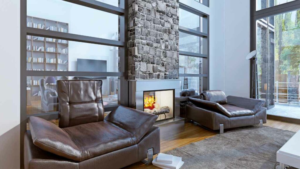 stone fireplace in a modern living room. Wood flooring. Leather chairs. Large windows. Wood burning fire.