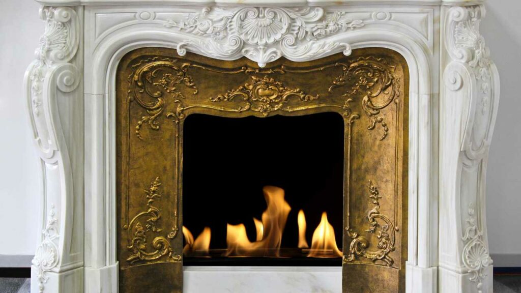 Decorative white marble fireplace. Also detailed gold fireplace surround with fire burning in the fireplace.