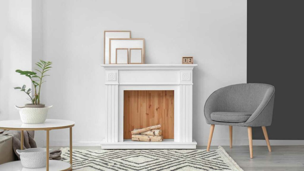 Modern Boho fireplace with log decor in empty fireplace. grey chair to the side and black and white rug on the floor in front. Mirrors on the mantle.