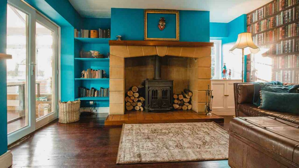 Boho styled fireplace, with rug in fron and wood either side of a large fire place. Blue walls with bookcase.