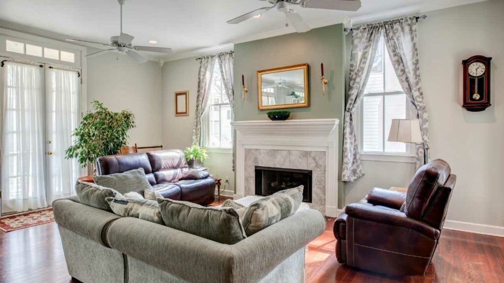 Mirror above fireplace. marble tiled fireplace surround. green walls. soafa and leather chairs. wood flooring windows either side of the fireplace