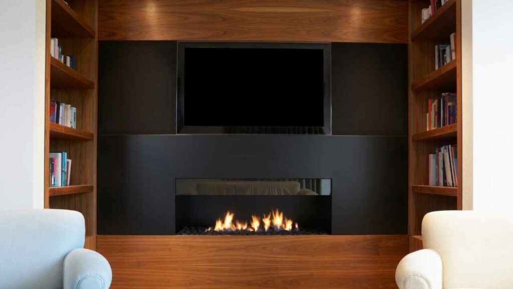TV above fireplace, built into wall. Wood surround. Book shelves either side of the fireplace.