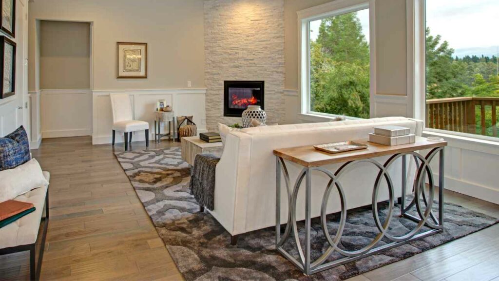 Corner fireplace used to divide room. Large rug on the floor and two large windows, Wood flooring.