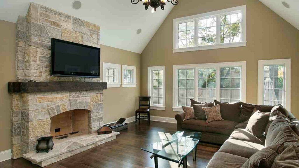 stone fireplace with tv above. wood flooring and L shaped sofa.