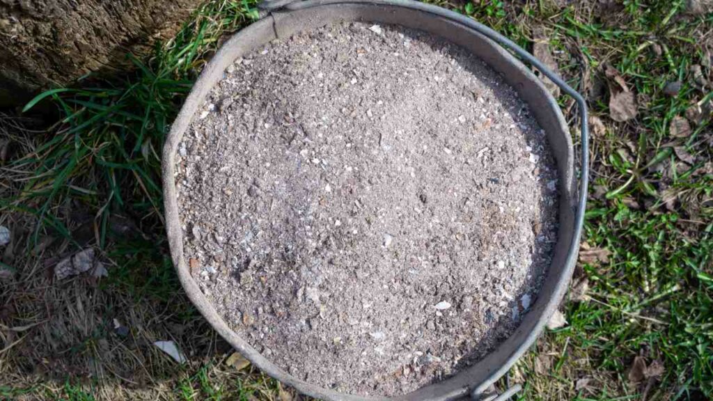 Metal bucket on the ground, nearly full with fireplace ash.