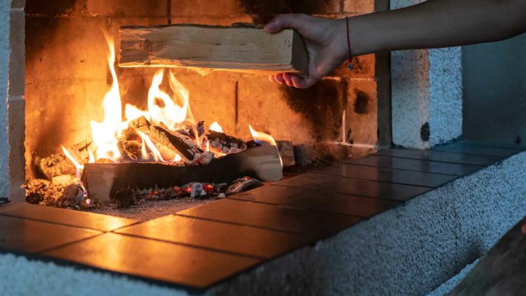 log being added to wood burning fireplace. Fire burning with kindling.