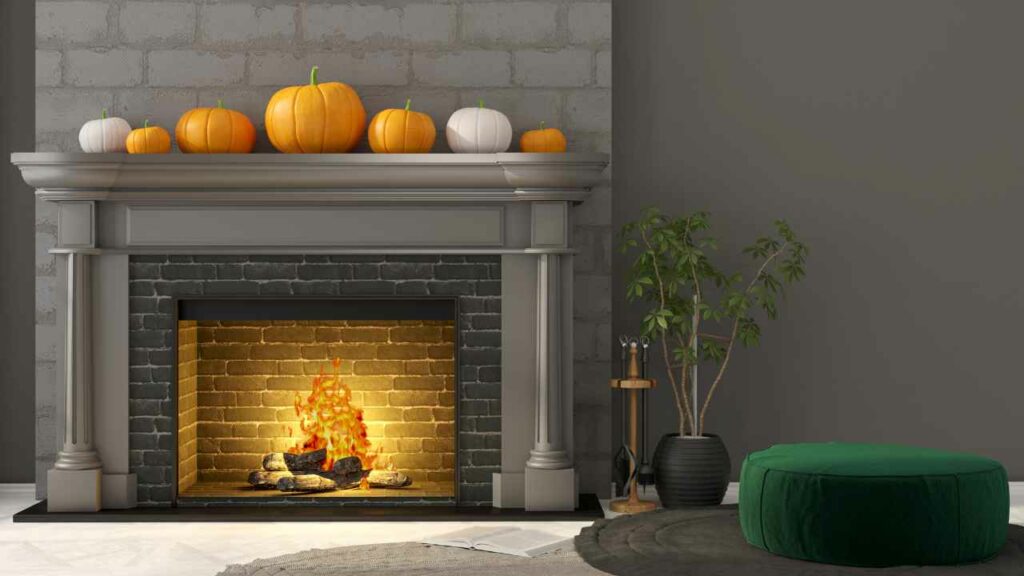 Red Brick fireplace, painted grey with halloween pumpking decorations on the mantel. Grey walls and grey fireplace surround. plant to one side. fire burning.