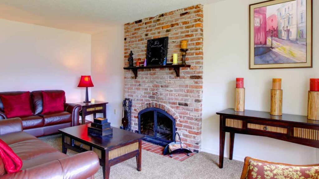 Red brick fireplace. Leather sofa in front. Shelf amntel above fireplace. 