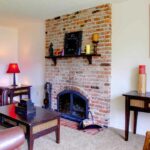 Red brick fireplace. Leather sofa in front. Shelf amntel above fireplace.