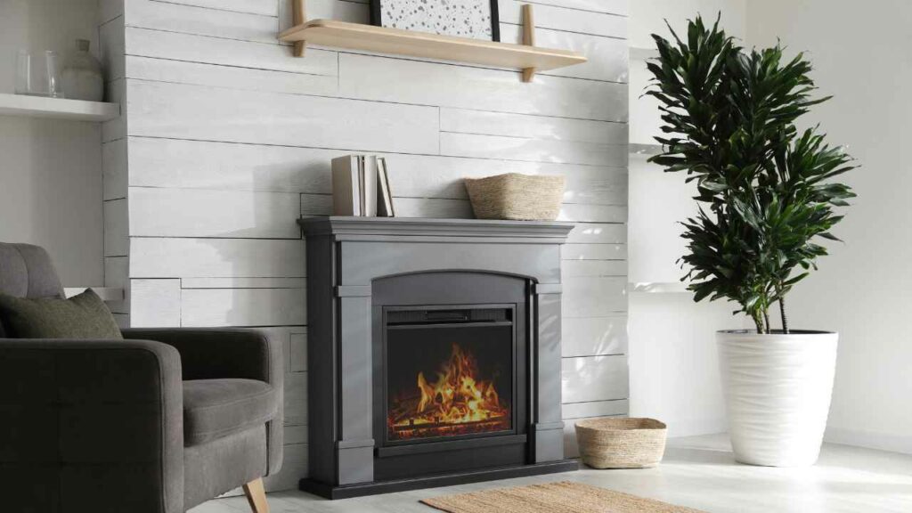 Elelctric fireplace. White walls. Grey Surround. Wood Shelf Above. Decorations on mantel.