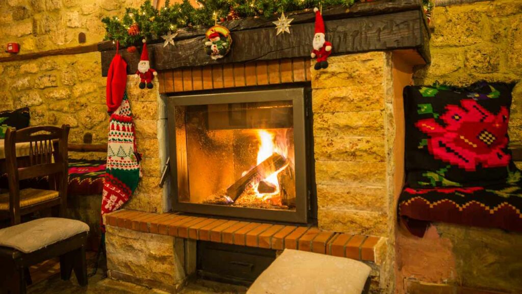 Mediteranean fstone fireplace. wood burning. christams decorations hanging from wood mantel. raised hearth of briosk and stone.