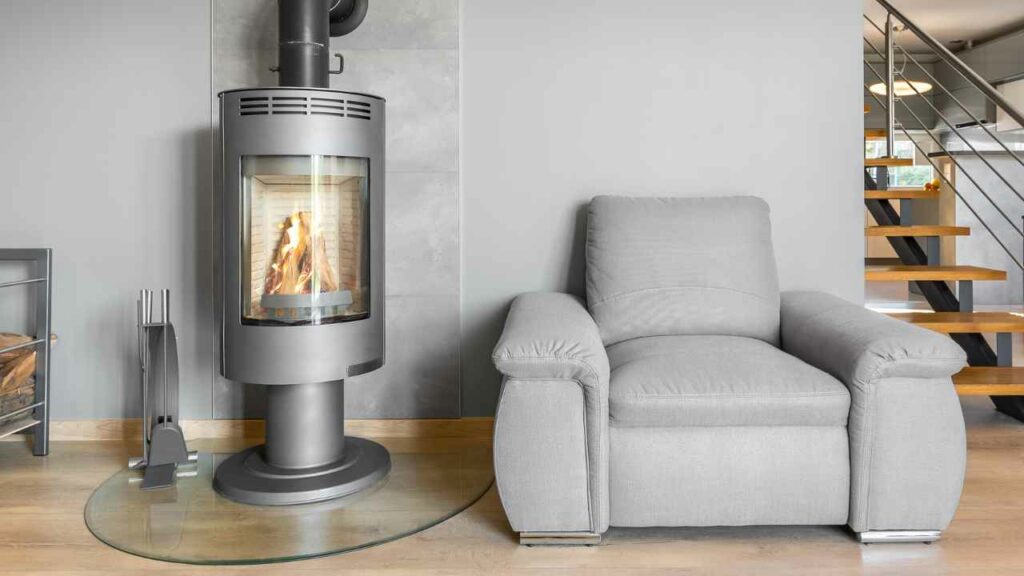Grey modern wood stove heater. Grey chair. Grey table. Wood floor. Grey walls.