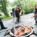 Oudoor wood burning fire pit with friends sitting on chairs and making smores