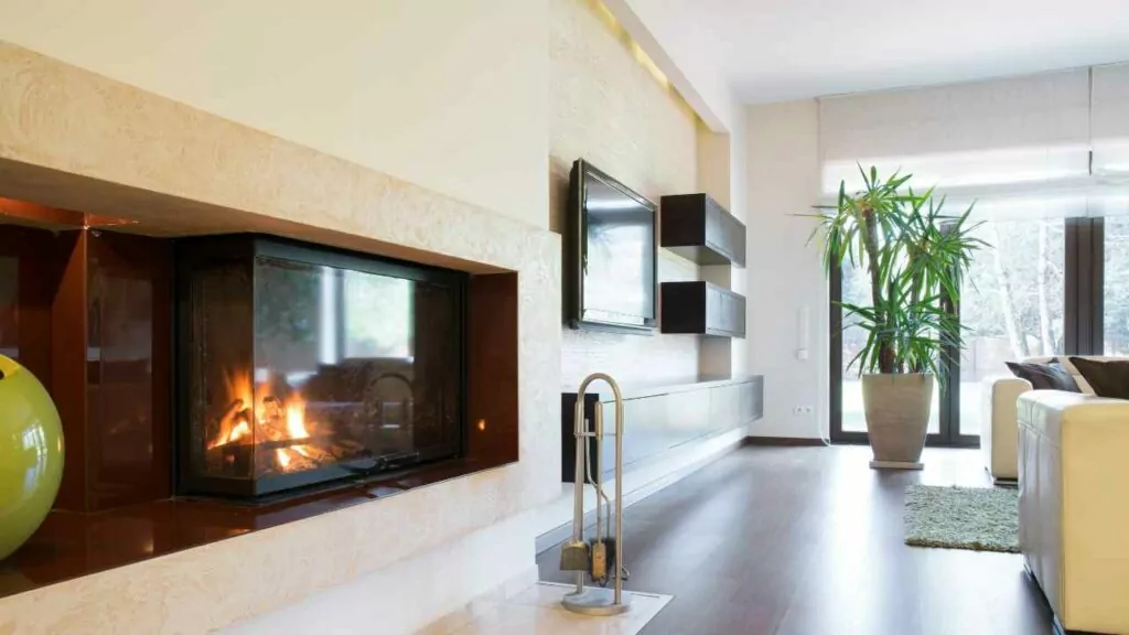 modern glass fronted wood burning fireplace. fireplace tools on the hearth. large modern living room. wood flooring. Wall TV.