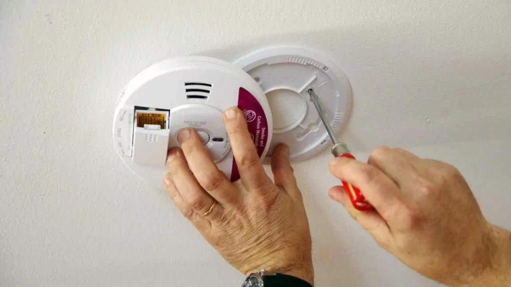 Smoke and Carbon Monoxide detector being fitted to the ceiling. Man using screwdriver to fix.