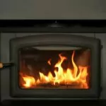 a wood burning fireplace insert. fire burning. black metal fire surround.