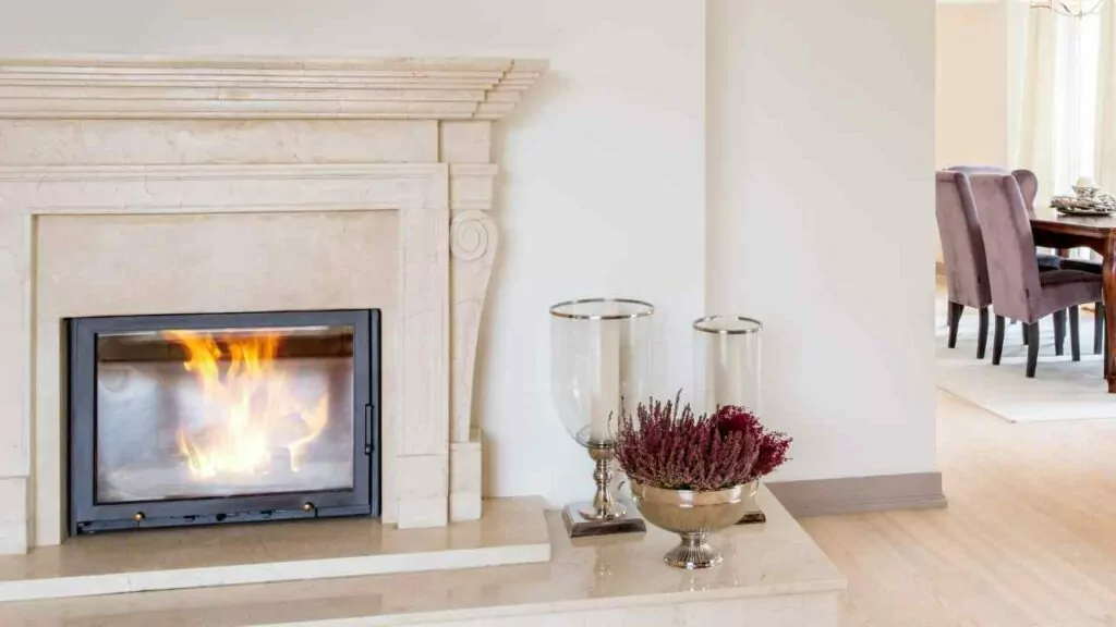 Cream marrble fireplace. Wood fire burning. Candles in front and marble hearth. Wood flooring.