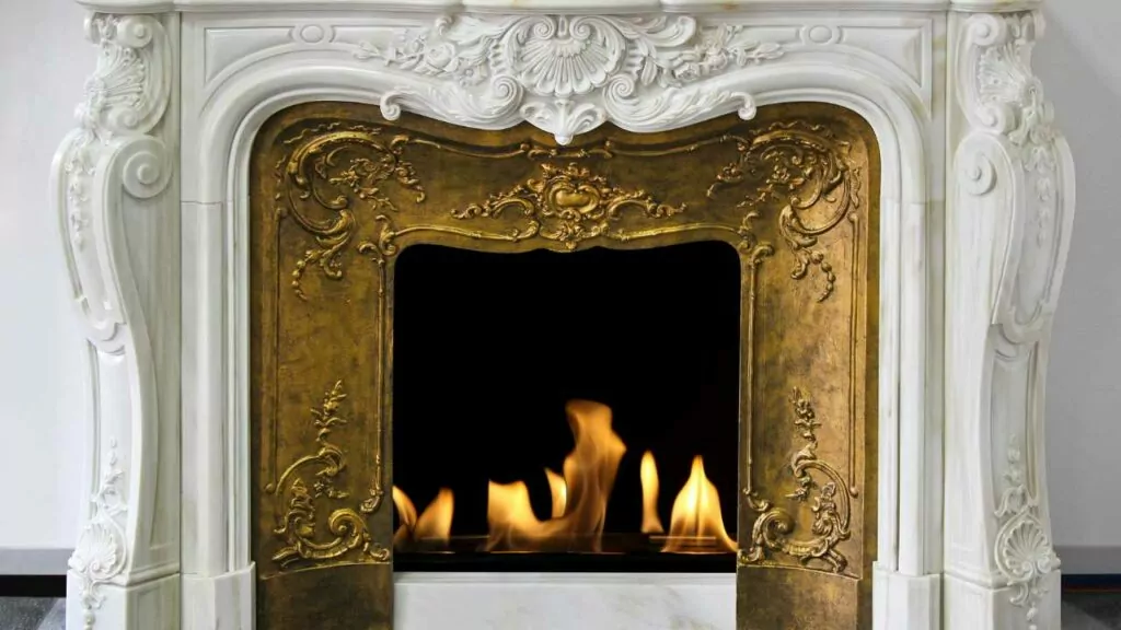 Decorative white marble fireplace. Also detailed gold fireplace surround with fire burning in the fireplace.