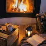 inset fireplace. wood flooring. basket with wood candle burning. book on the floor.