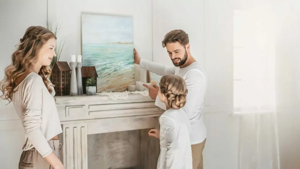 art being added to the wall above a fireplace. parents and child looking at the painting.