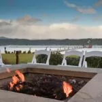 Square Fire Pit with wood bunring. plastic chaor and view of the river.