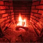 red brick fireplace with two logs burning.