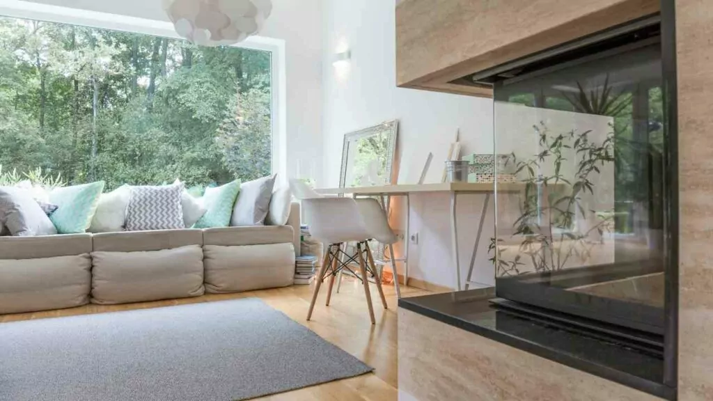 Corner wood burning fireplace. modern looking living room. wood flooring. white walls. rug on the floor.