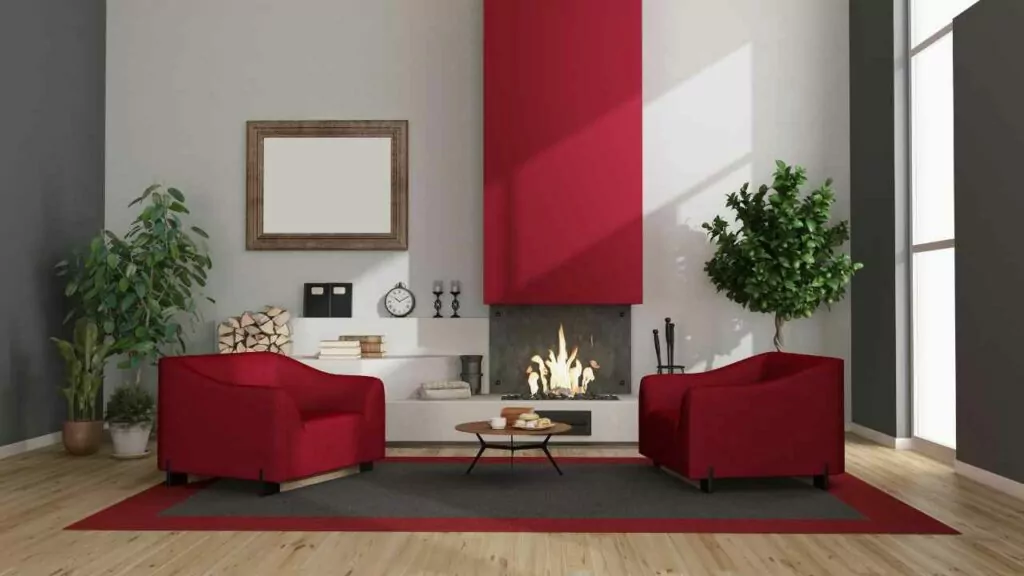 Two red chairs either side of a fireplace. red chimney beast. wood flooring. rug on floor.